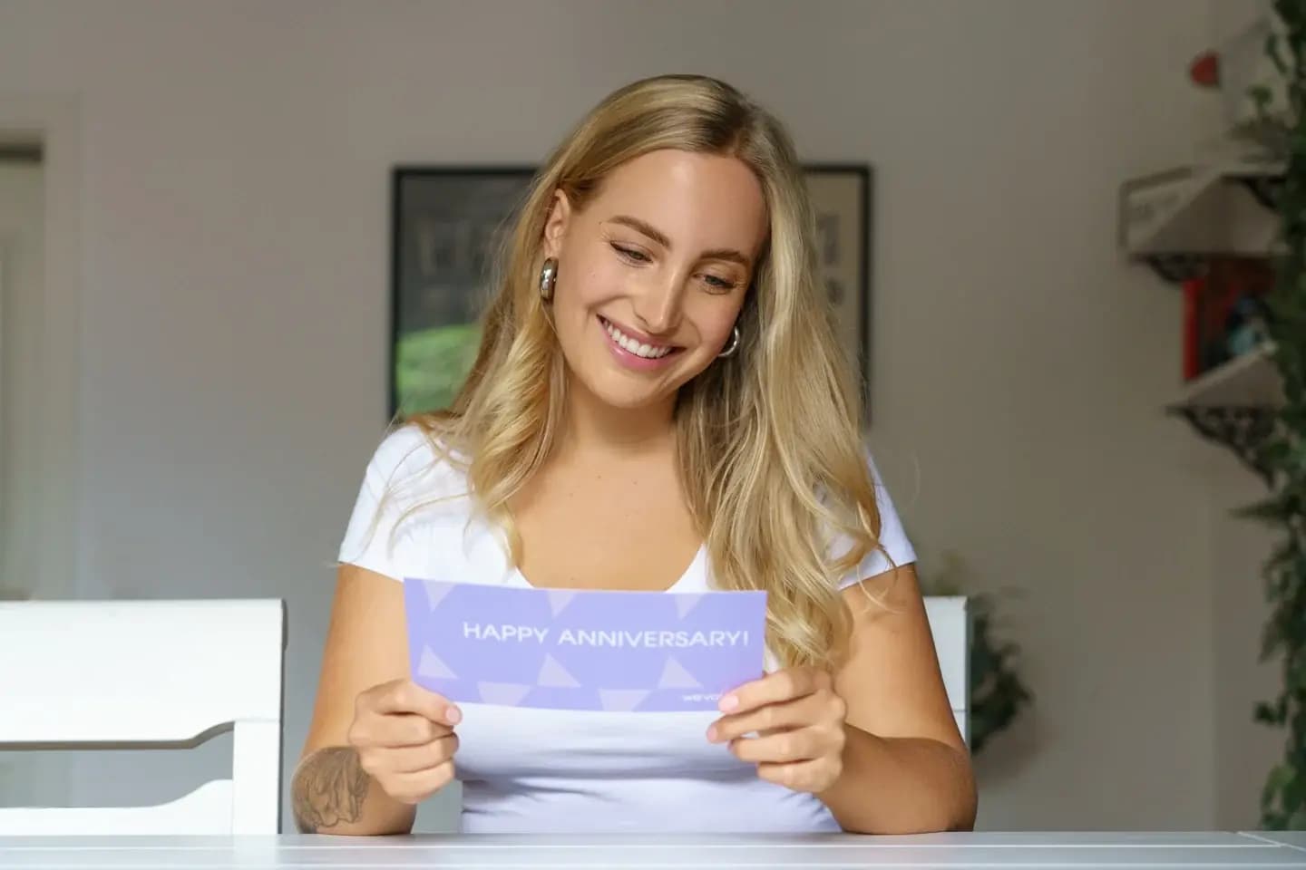 Eine Frau liest lächelnd eine Happy-Anniversary-Grußkarte von thevalyoubox